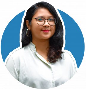 A circular headshot of Faaqiah, set against a solid blue background providing a clean professional look. Faaiqah has long black hair, wearing spectacles and big hoop earrings. She's wearing a white-collared long sleeve top.